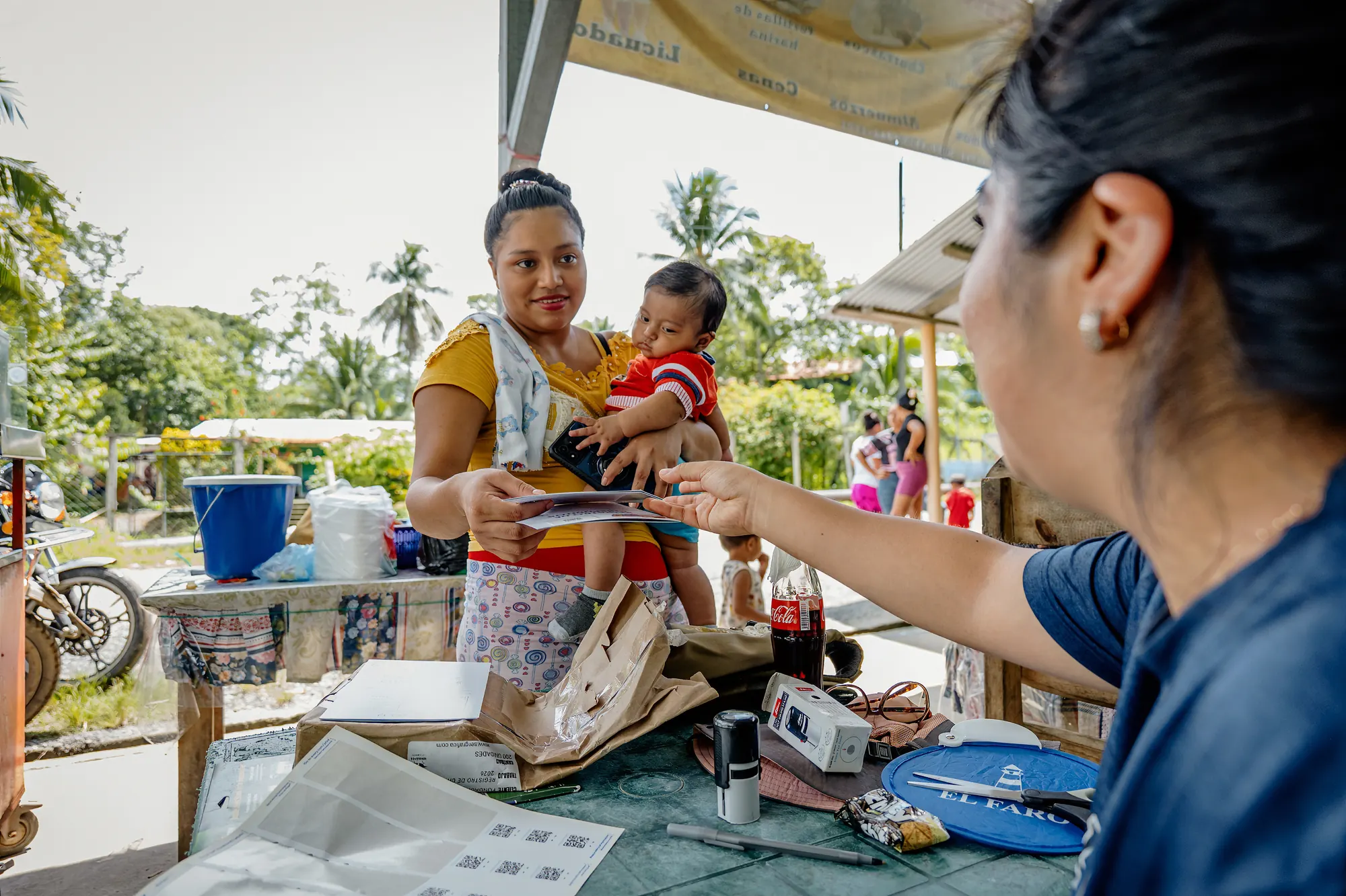 An El Faro team member distributes nutrition support to a mother and child.