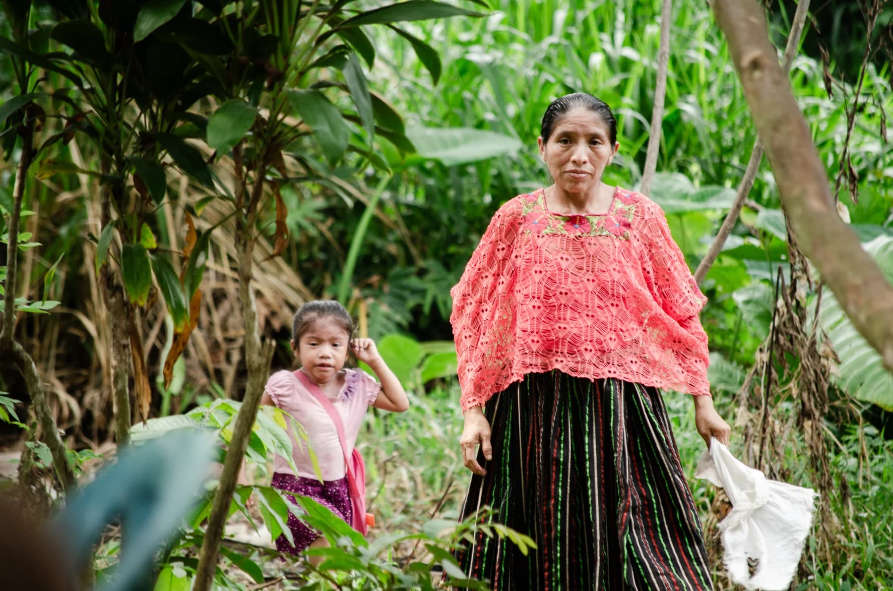 Una mujer y una niña caminan por un sendero tropical.